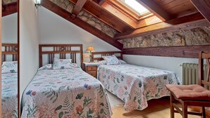 Un dormitorio con dos camas, tragaluces, vigas de madera y una pared de piedra.