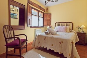 A bedroom with a wooden bed, a chair, a window with a view, and a nightstand with a lamp.