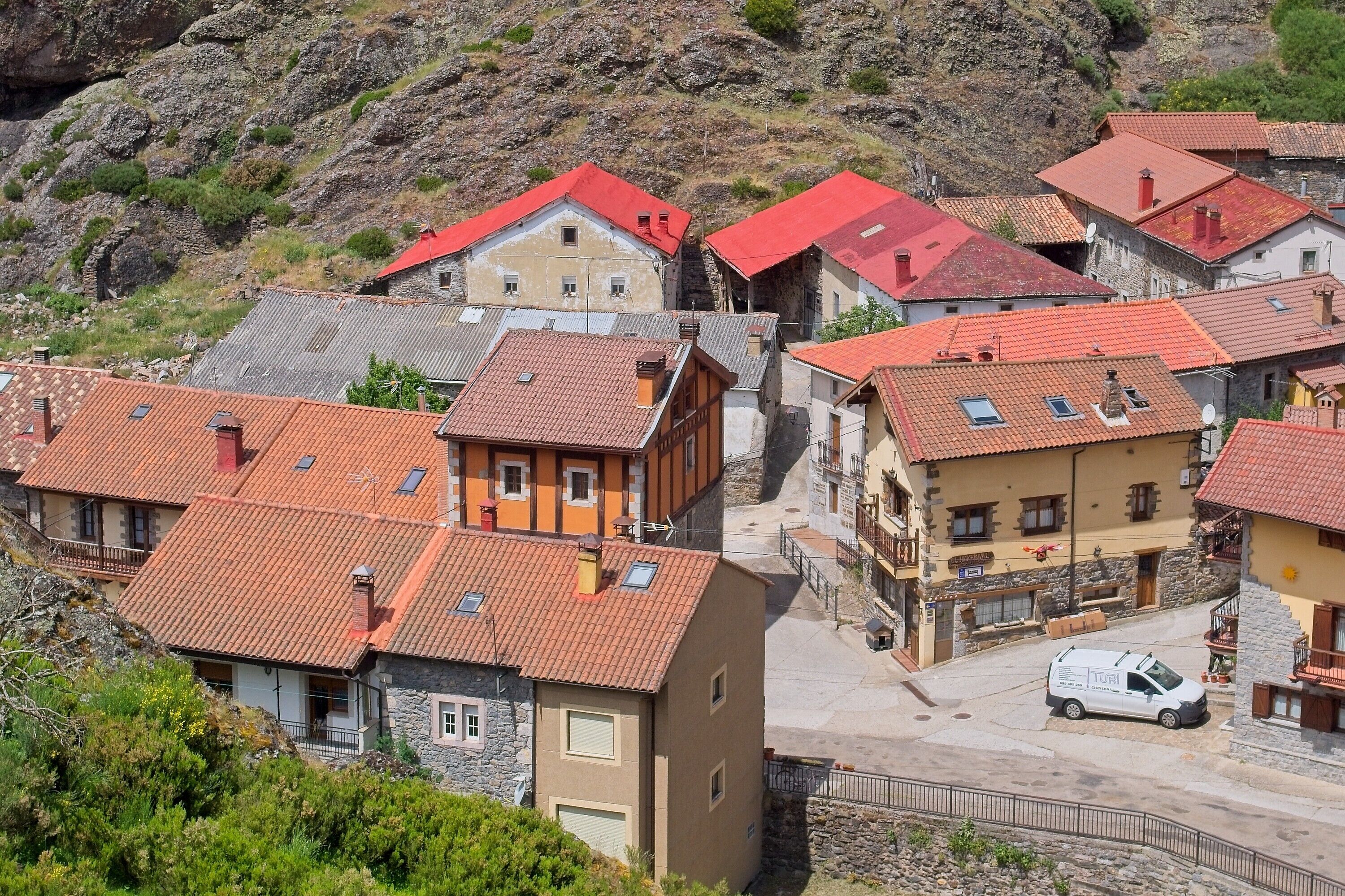 A cluster of traditional buildings with red-tiled roofs, a stone pathway, and a parked van.