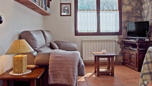Ein gemütliches Wohnzimmer mit einer Couch, einer Lampe, einem Fernseher, einem Kamin und einem Fenster mit Vorhängen.