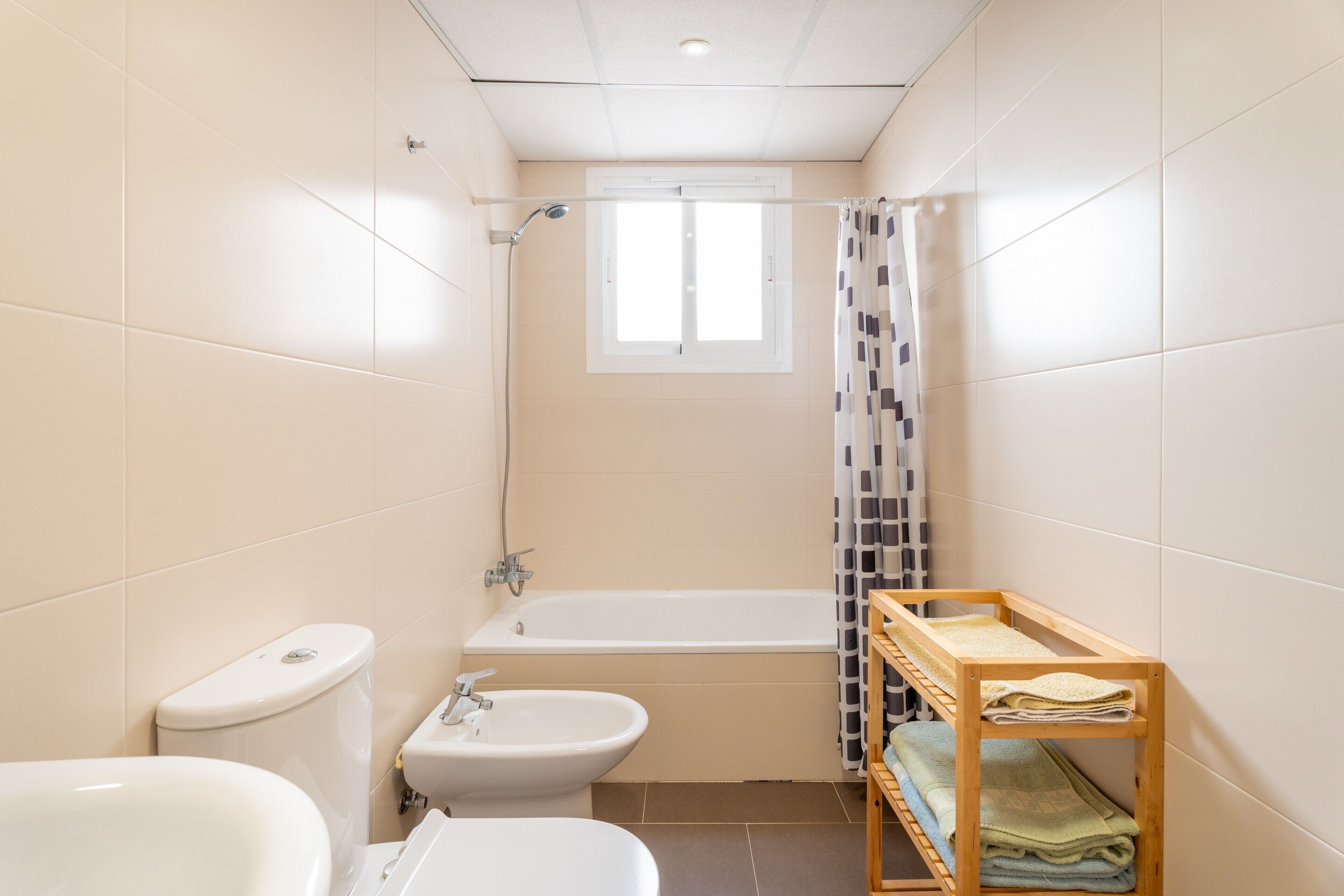 Ein Badezimmer mit Toilette, Bidet, Waschbecken, Badewanne und einem Holzregal mit Handtüchern.