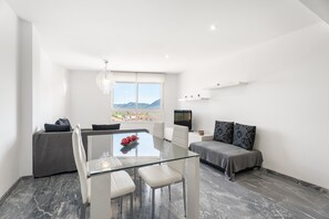 Uma sala de estar moderna com uma mesa de jantar de vidro, um sofá, uma televisão e vista para as montanhas.