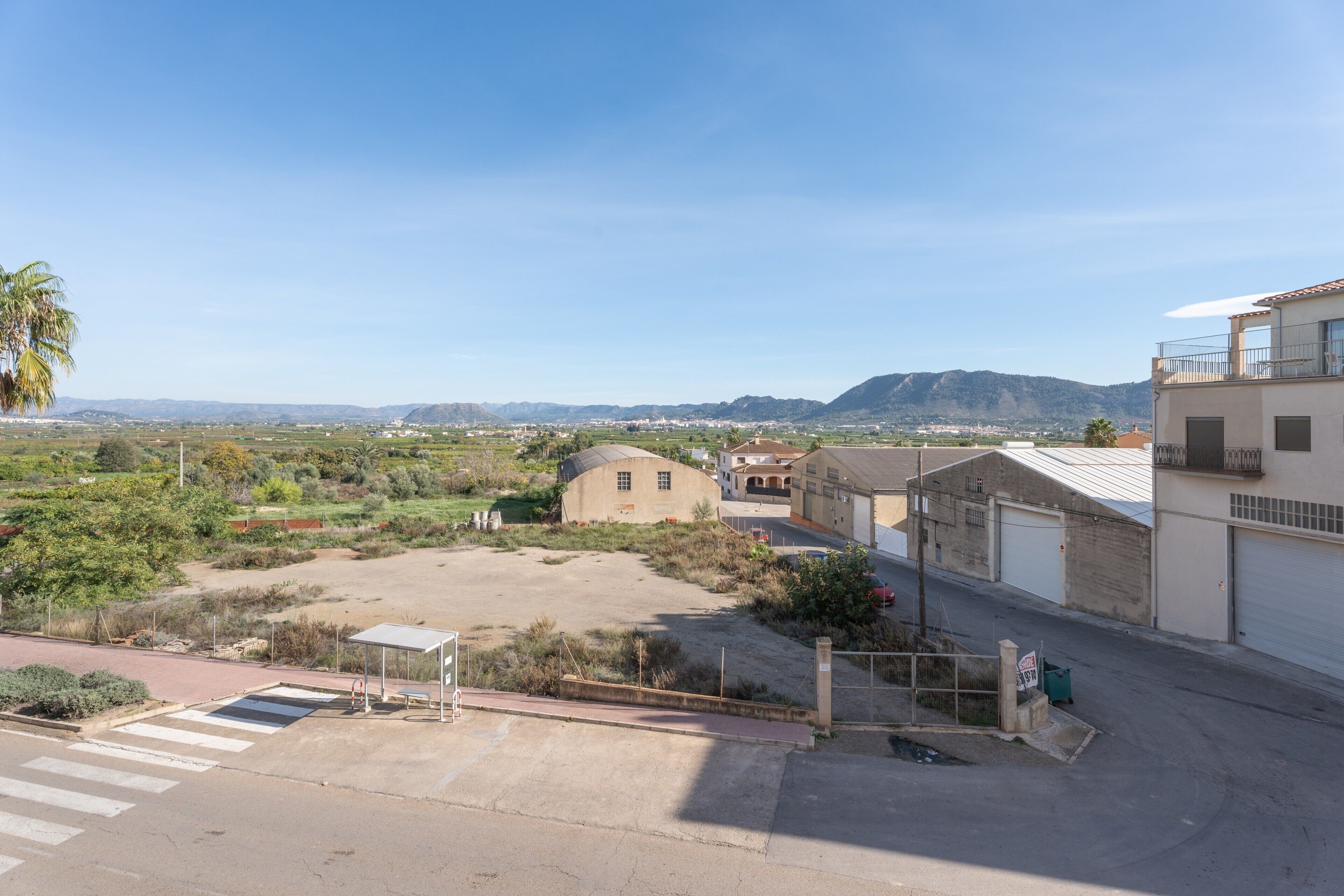 Zona residencial com rua pavimentada, um pequeno edifício e montanhas ao longe.