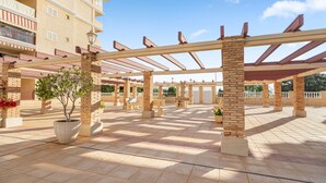Ett takförsett utomhusområde med en pergola, krukväxter och en byggnad med balkonger.
