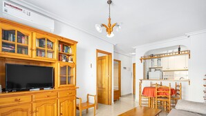 Ett vardagsrum med en TV, träskåp, ett matbord och en köksdel.