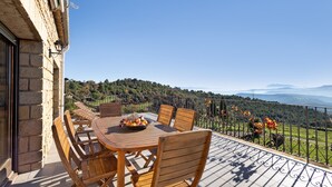 A terrace with a table and chairs, a view of a mountainous landscape, and a stone building.