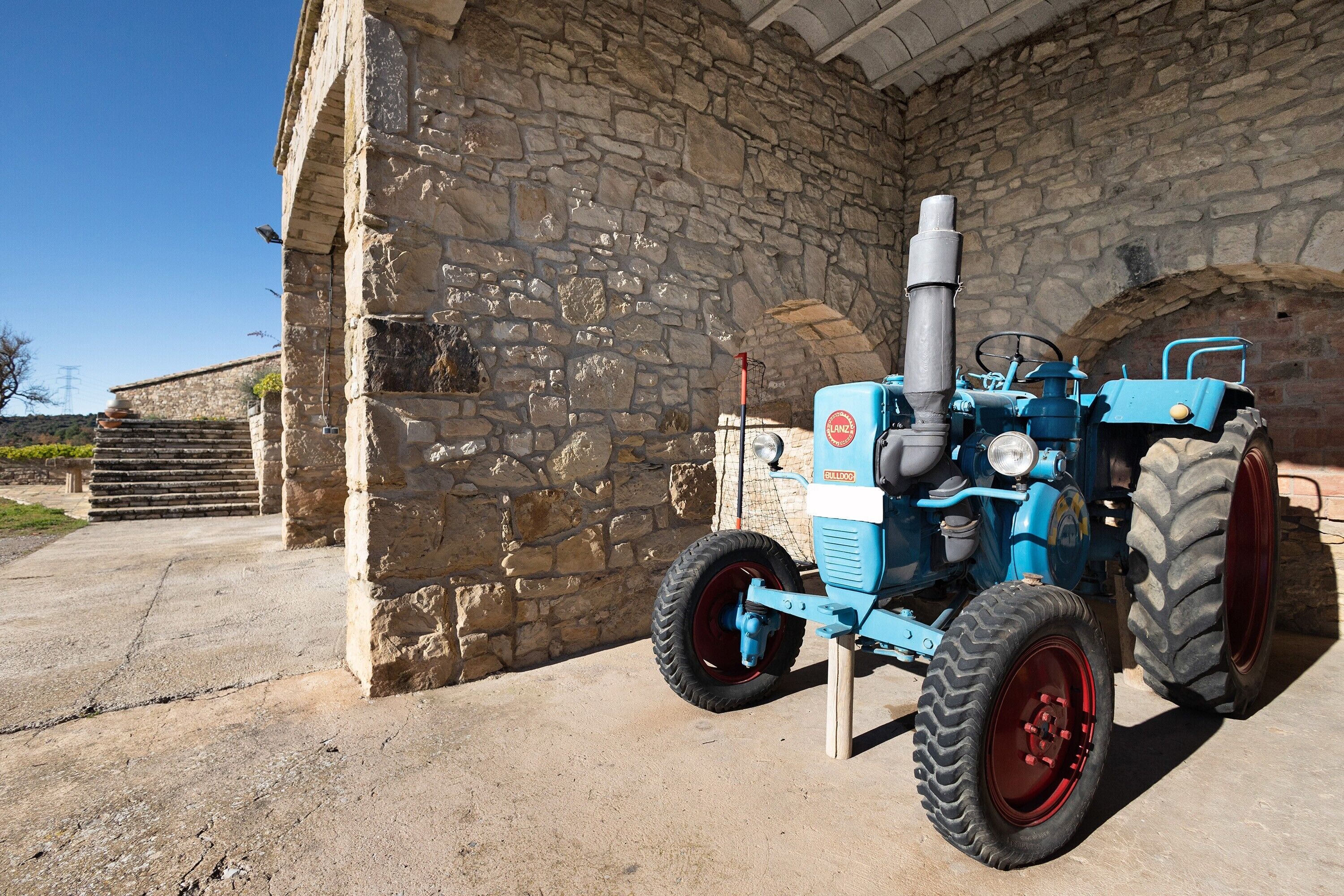 A blue tractor parked outside a stone building with a metal gate.