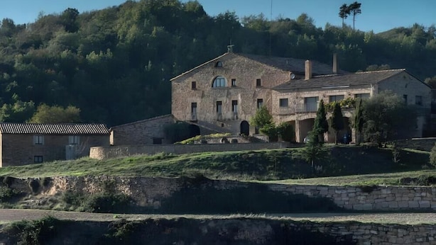A stone building with a central archway, surrounded by greenery and hills.