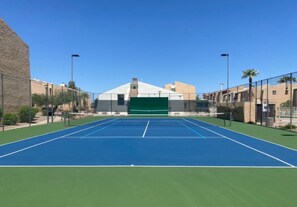 Ein Tennisplatz im Freien mit grüner und blauer Belag, umgeben von Gebäuden und Palmen.