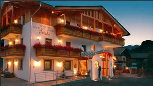 Un immeuble à deux étages doté de balcons ornés de fleurs rouges, une enseigne indiquant qu’il s’agit d’une résidence et d’un restaurant, et une entrée accueillante.