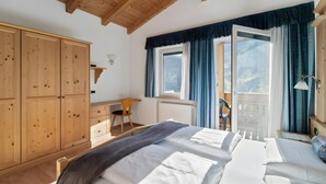 Une chambre à coucher comprenant un lit, une armoire en bois, un bureau, une chaise et un balcon avec des rideaux.