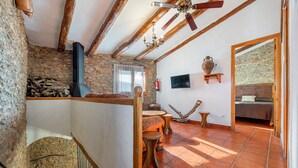 A rustic room with stone walls, a fireplace, wooden furniture, and a tiled floor.