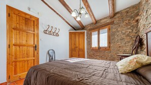 A bedroom with a large bed, wooden doors, stone walls, and a chandelier.