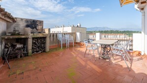 A rooftop terrace with a table and chairs, a grill, and a view of distant mountains.