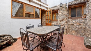 A courtyard with a stone wall, a wooden door, and a tiled patio with a metal table and chairs.