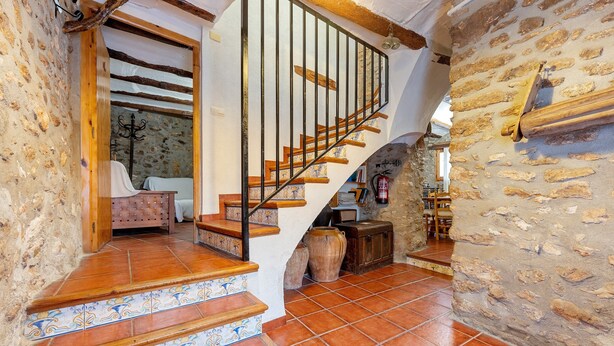 A staircase with wooden steps and a metal railing, leading to a room with a white ceiling and a stone wall.