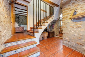 Una escalera con escalones de madera y barandilla de metal, que conduce a una habitación con techo blanco y pared de piedra.