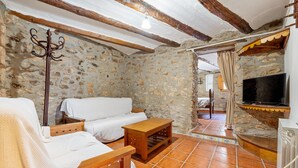 A rustic stone-walled room with a white sofa, wooden furniture, a TV, and a stone fireplace.