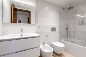 A modern bathroom with a shower, toilet, bidet, and a large mirror.