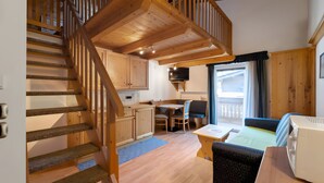Un escalier en bois mène à une chambre aménagée en mezzanine, où se trouvent un lit, un bureau et un téléviseur.