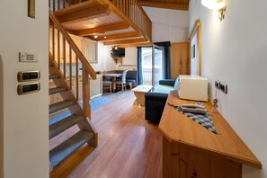 Una escalera de madera conduce a un dormitorio en un altillo, un comedor con mesa y sillas, y una kitchenette con microondas y tostadora.