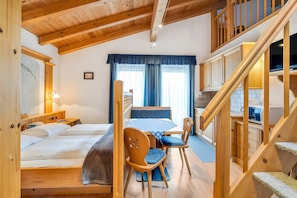 A wooden interior with a bed, a dining table with chairs, a kitchen area, and a staircase.