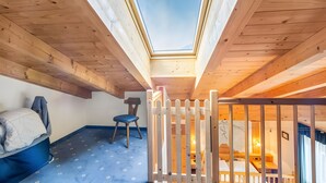 Ein Zimmer mit Oberlichter, Holzbalken, einem Bett und einem Stuhl, sowie einem weißen Zaun.
