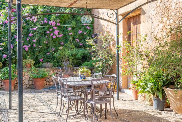 An outdoor patio with a table and chairs, surrounded by potted plants and a stone wall.