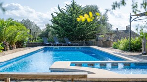 A rectangular swimming pool with a stone border, surrounded by lounge chairs and greenery. - Country House 'S' Oratge' with Mountain View, Shared Pool and Wi-Fi (Illes Balears)
