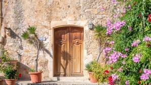 A stone building with a wooden double door, potted plants, and a sign. - Country House 'S' Oratge' with Mountain View, Shared Pool and Wi-Fi (Illes Balears)