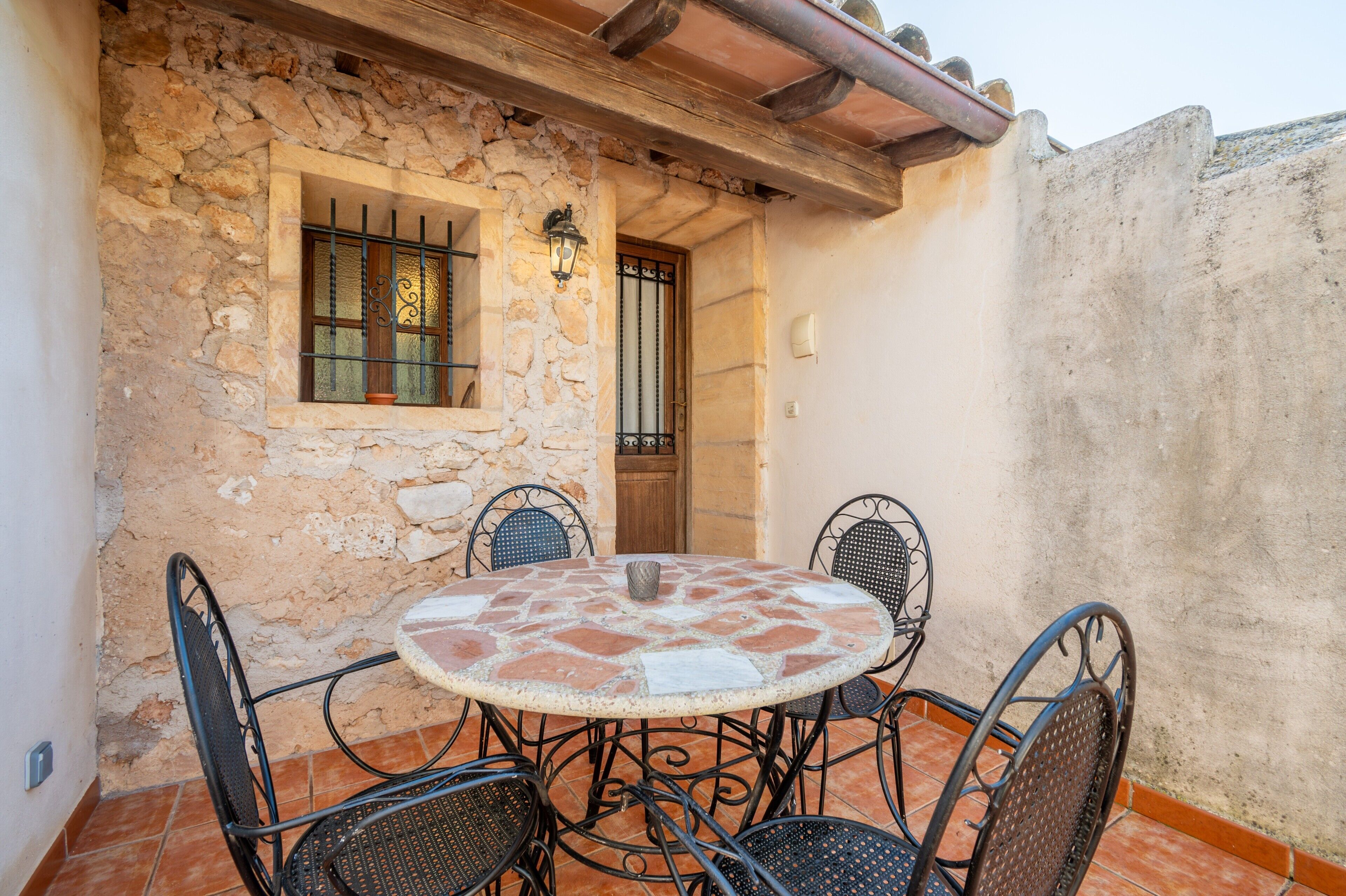 A stone wall with a window and door, a round table with chairs, and a tiled floor.