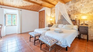 A bedroom with a bed, bedside tables, a bench, a window, and a stone wall. - Country House 'S' Oratge' with Mountain View, Shared Pool and Wi-Fi (Illes Balears)