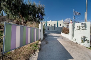A pathway leading to a building with a white facade, a flag, and a statue.