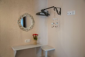A bathroom with a mirror, a hanging light fixture, a small shelf with a vase of flowers, and a wall-mounted electrical outlet. - Apartment 'Studios Kapsali 3' with Sea View, Wi-Fi and Air Conditioning (Galini)