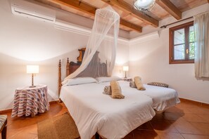 Un dormitorio con dos camas, dosel, mesita de noche con lámpara y ventana con cortinas.
