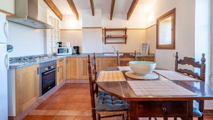 Een keuken met houten keukenkastjes, een gasfornuis, een magnetron en een eethoek met een tafel en stoelen.