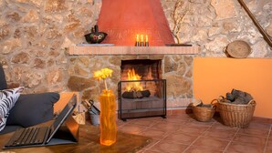 A stone wall, a fireplace with logs, a laptop on a table, and wicker baskets. - Country House 'Casa Rural Angelita' with Mountain View, Wi-Fi and Air Conditioning (Rossell)