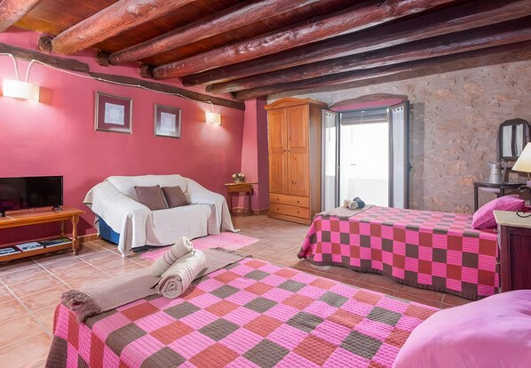 A room with a wooden ceiling, a bed with a pink quilt, a TV, and a stone wall.