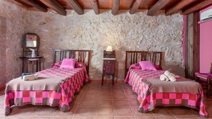 A room with two beds, stone walls, wooden beams, a small table with a lamp, and a chair. - Country House 'Casa Rural Angelita' with Mountain View, Wi-Fi and Air Conditioning (Rossell)