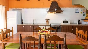 A kitchen with wooden cabinets, a dining table with chairs, a fruit bowl, and a microwave. - Country House 'Casa Rural Angelita' with Mountain View, Wi-Fi and Air Conditioning (Rossell)