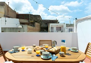 A breakfast table set on a balcony with a city view, including buildings and a clear sky.