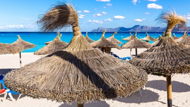 Een strand met rieten parasols en een heldere blauwe zee.