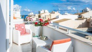 Een balkon met witte rieten meubels, een potplant en uitzicht op de stad.