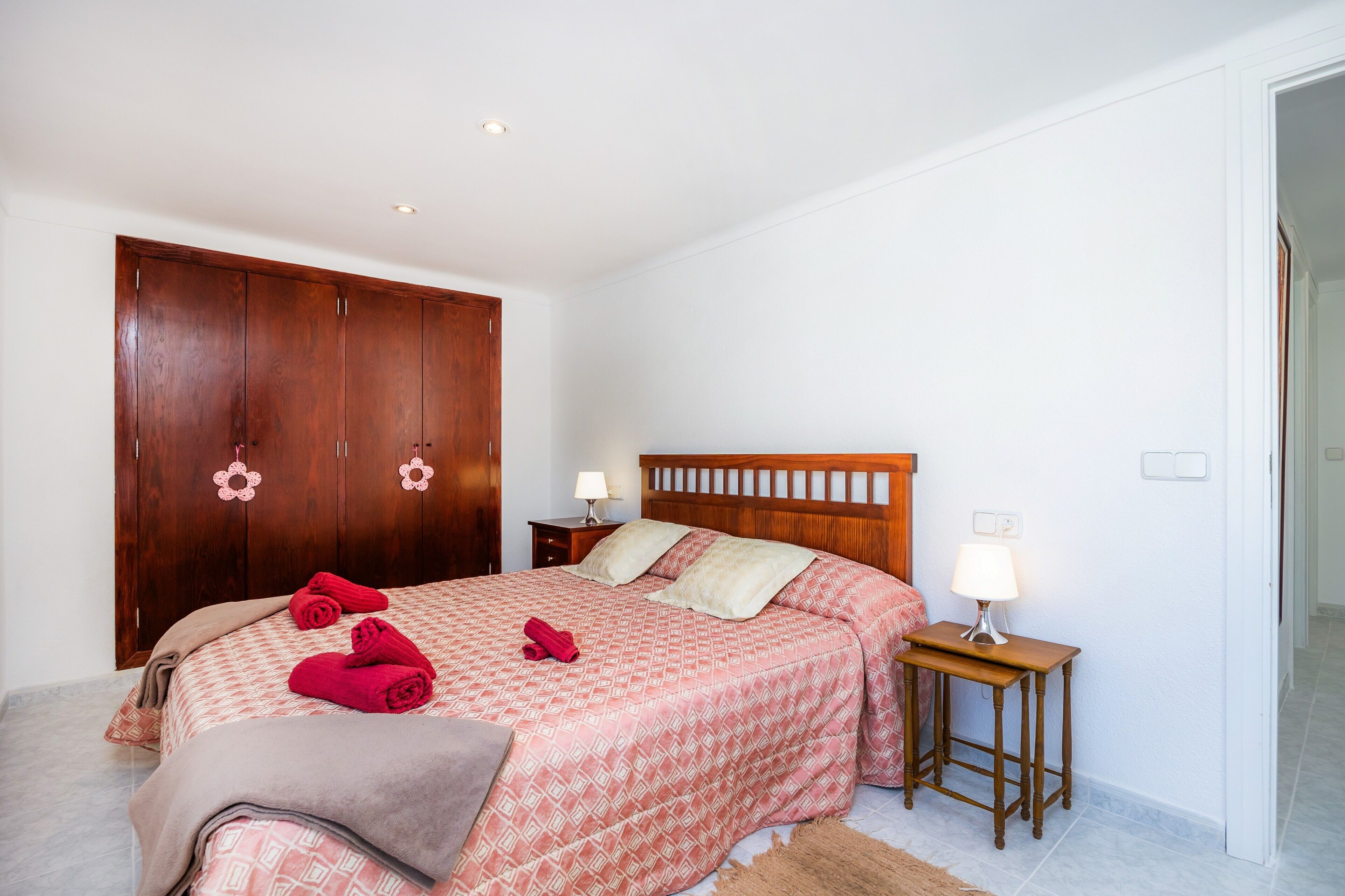 Ein Schlafzimmer mit einem Bett, einem Holzschrank, einem Nachttisch mit Lampe und einem Teppich.