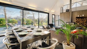 A modern dining area with a long table, chairs, and a view of the outdoors. - Holiday Home 'Mézon Ermine' with Terrace, Private Garden and Wi-Fi (Saint-Cast-le-Guildo)