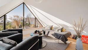 A modern loft bedroom with a large window, a bed, a sofa, and a coffee table. - Holiday Home 'Mézon Ermine' with Terrace, Private Garden and Wi-Fi (Saint-Cast-le-Guildo)