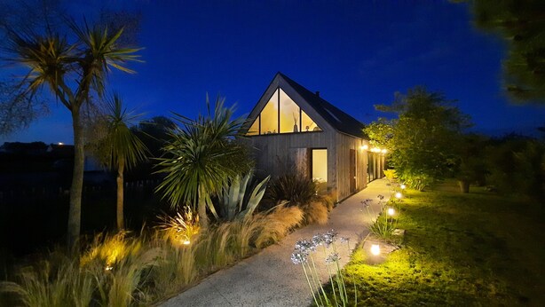A modern house with a large glass window, surrounded by tropical plants and a well-lit pathway. - Holiday Home 'Mézon Ermine' with Terrace, Private Garden and Wi-Fi (Saint-Cast-le-Guildo)