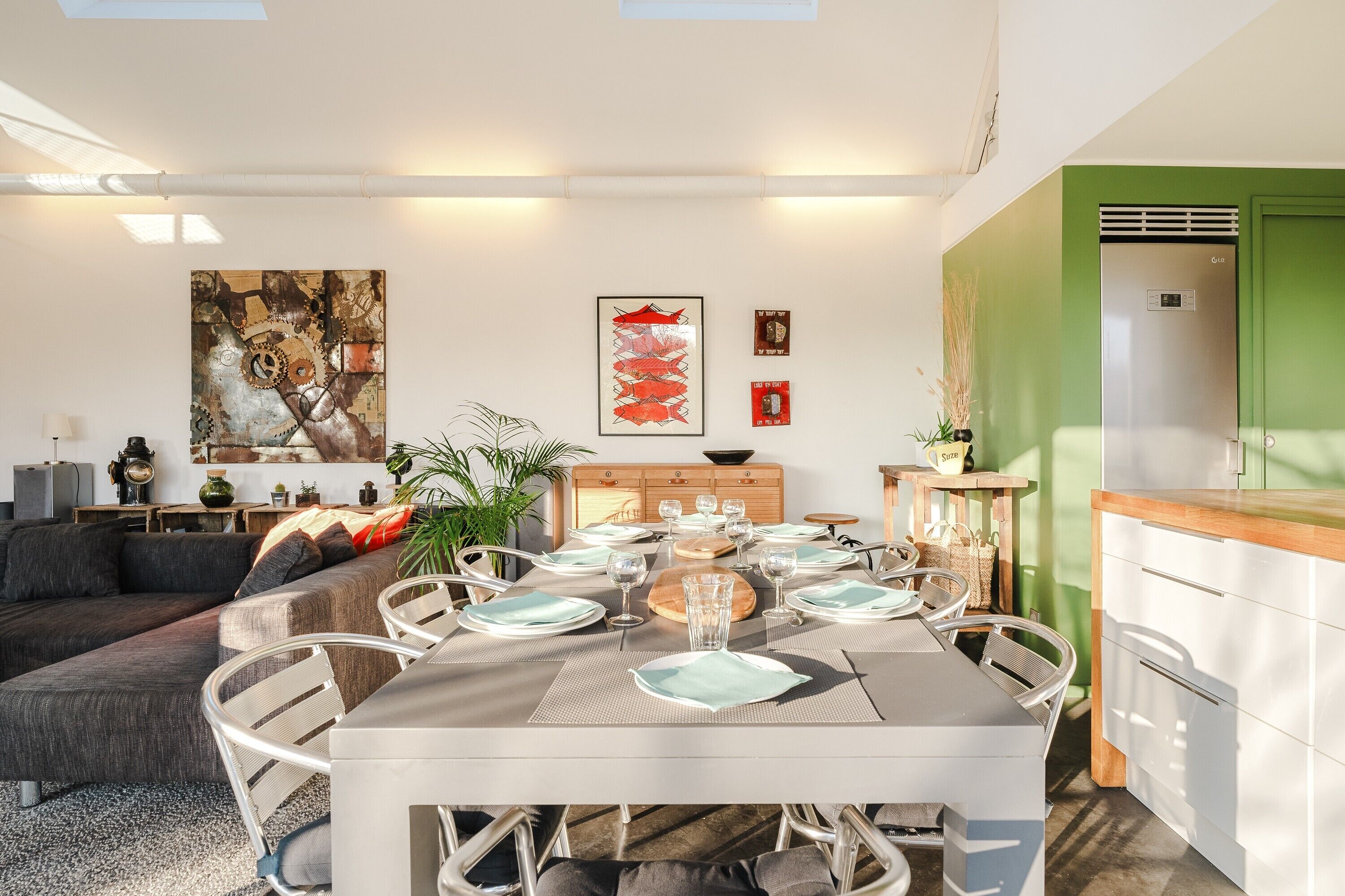 A modern dining area with a table set for four, a sofa, and a green accent wall.
