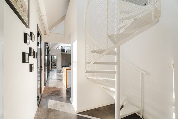 A modern interior with a staircase, a hallway with framed pictures, and a dining area.