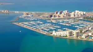Vista aérea de uma marina com vários barcos, edifícios altos adjacentes e um mar azul e límpido.